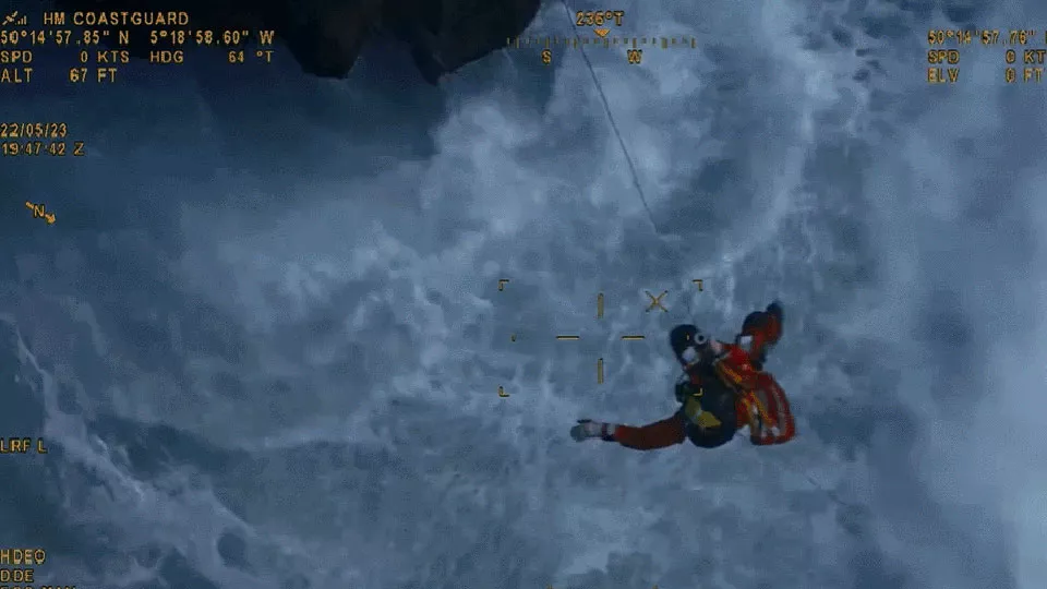 A Coastguard winchman hangs from the winch above a choppy sea