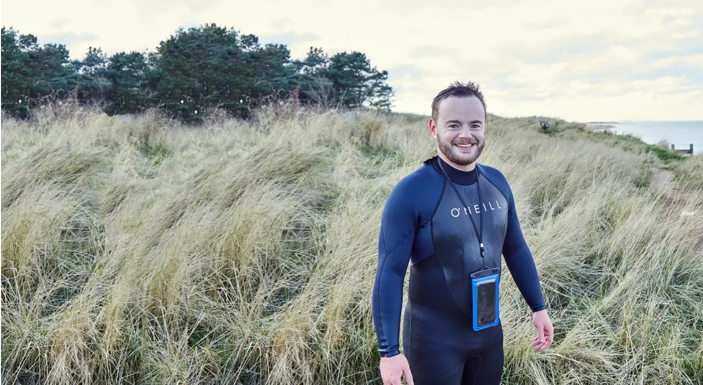 Surfer in a wet suit standing in tall grass by the sea