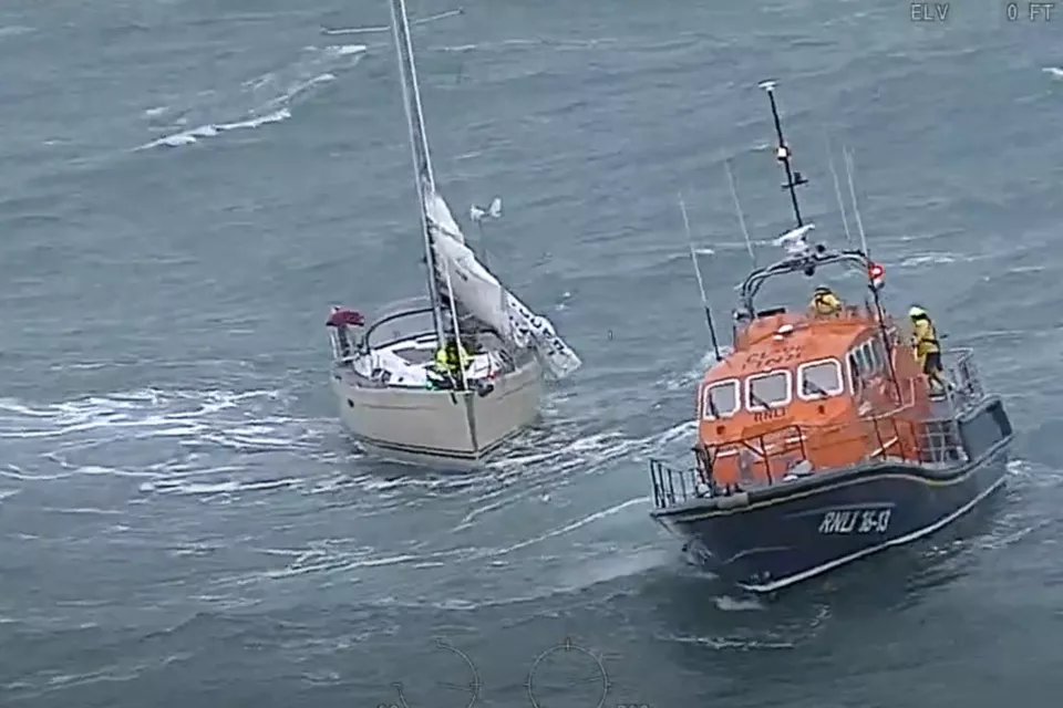 White sailing yacht and orange and blue RNLI vessel in stormy waters